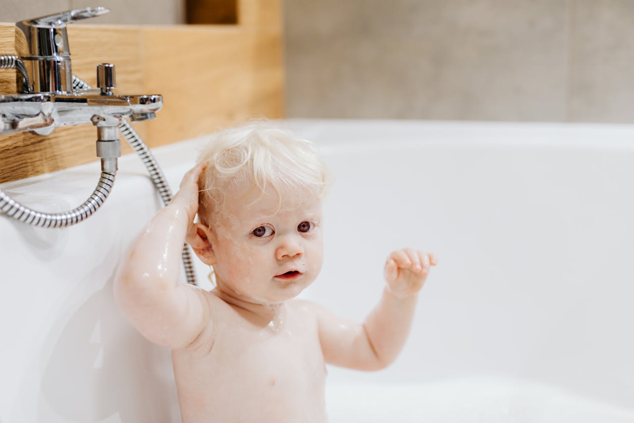 Cute toddler with blonde hair enjoying bath time with bubbles in a cozy bathroom.